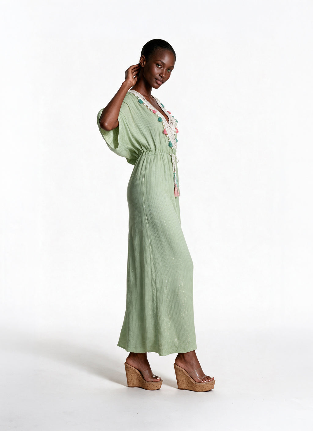A woman modeling a sage green maxi dress with a floral embroidered neckline, standing against a plain white studio background.