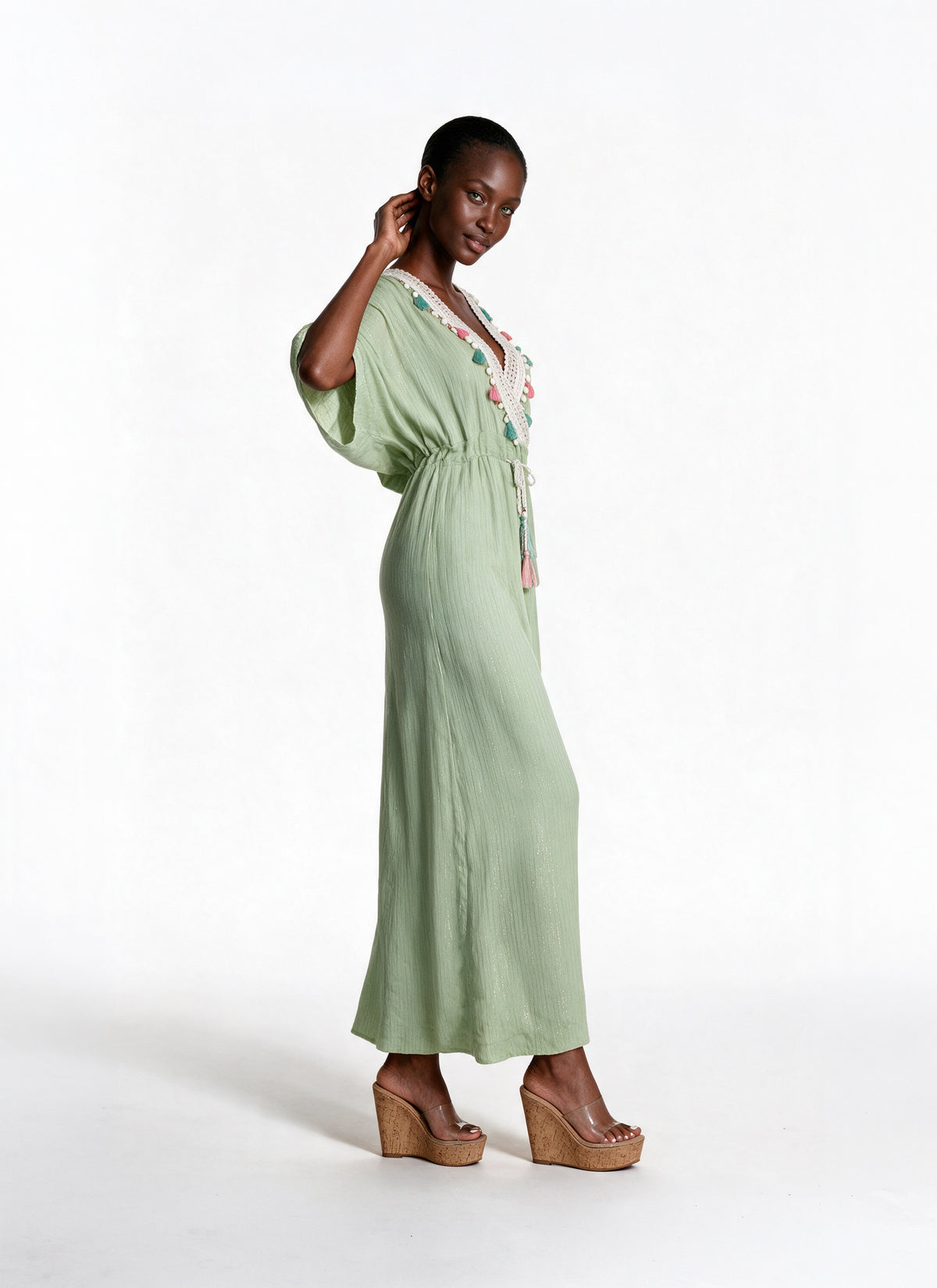 A woman modeling a sage green maxi dress with a floral embroidered neckline, standing against a plain white studio background.