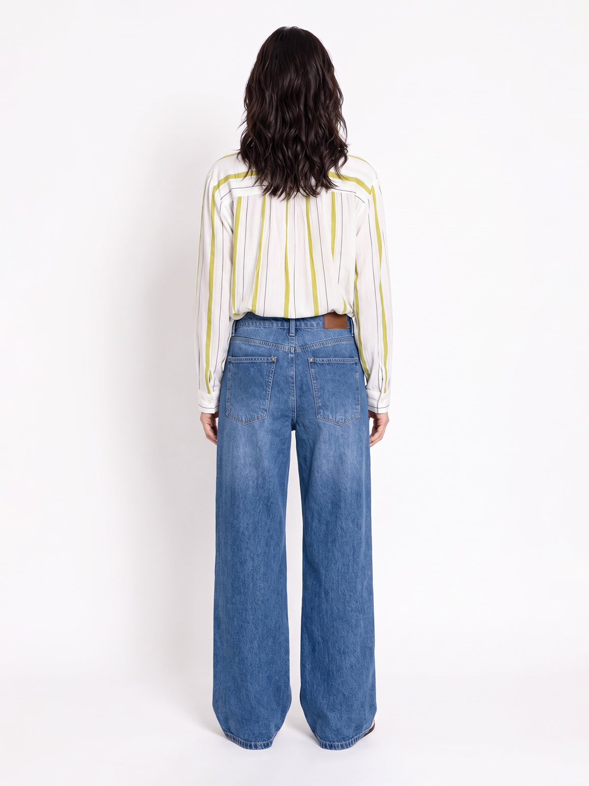 A model viewed from the back wearing a cream long-sleeve shirt with thin yellow vertical stripes and high-waisted, wide-leg blue denim jeans against a plain white studio background.