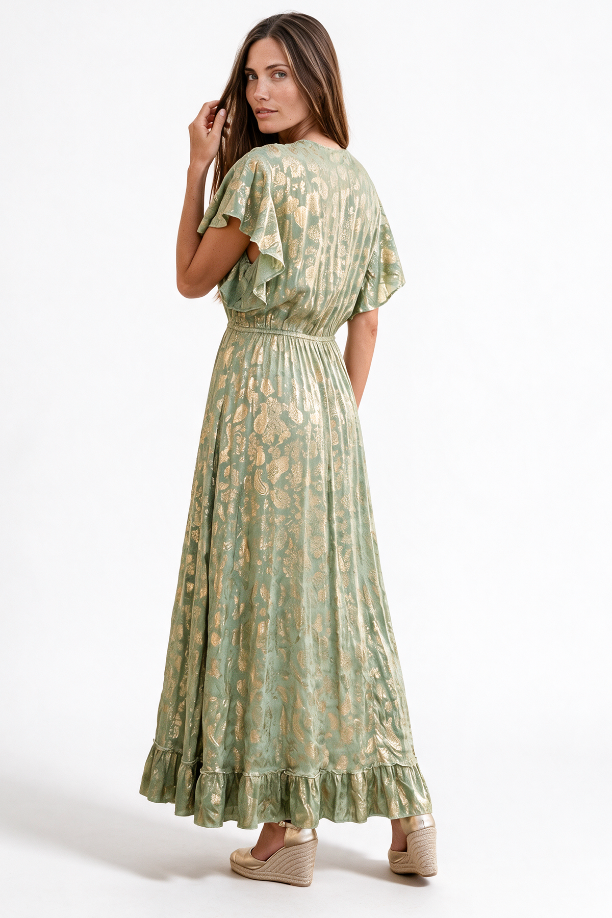 A woman modeling a sage green maxi dress with a gold floral pattern, shown from the back against a plain white studio background.